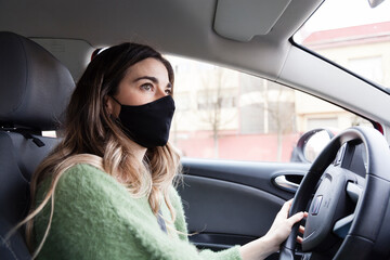 Young white spanish woman wearing protective mask and while driving and green sweater while driving a car. Health care, coronavirus, influenza and epidemics driving stills.