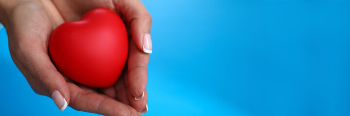 Close-up of female hands holding red heart on blue background. Motherhood and protection. Copy space. Family relationship and charity and adoption concept
