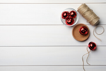 Naklejka na ściany i meble Red sleigh bells and rope on white wooden background, flat lay. Space for text