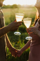 Glasses of champagne close-up in the hands of a woman and a man in nature at sunset.