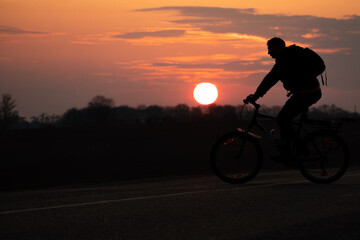 The silhouette of a cyclist against the background of the sun and the beautiful sky. The outline of a man riding on a bicycle against the background of the sunset.