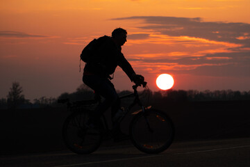 Obraz premium The silhouette of a cyclist against the background of the sun and the beautiful sky. The outline of a man riding on a bicycle against the background of the sunset.