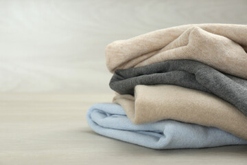Stack of cashmere clothes on wooden table. Space for text
