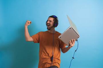 Young handsome man with gamer headphone set isolated over blue background using laptop computer playing a game. © deliris