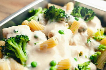 Freshly cooked pasta, broccoli and peas, covered in sauce, in a pan, ready to bake, healthy food