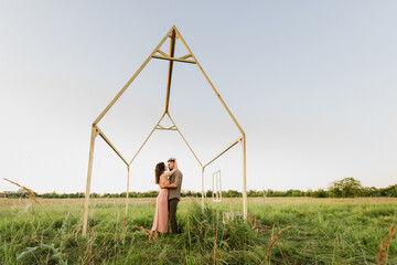 Young handsome men and women hug and kiss near the house in the field.