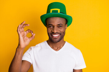 Portrait of positive afro american guy enjoy saint patrick celebration show ok sign wear green hat white t-shirt isolated over bright shine color background