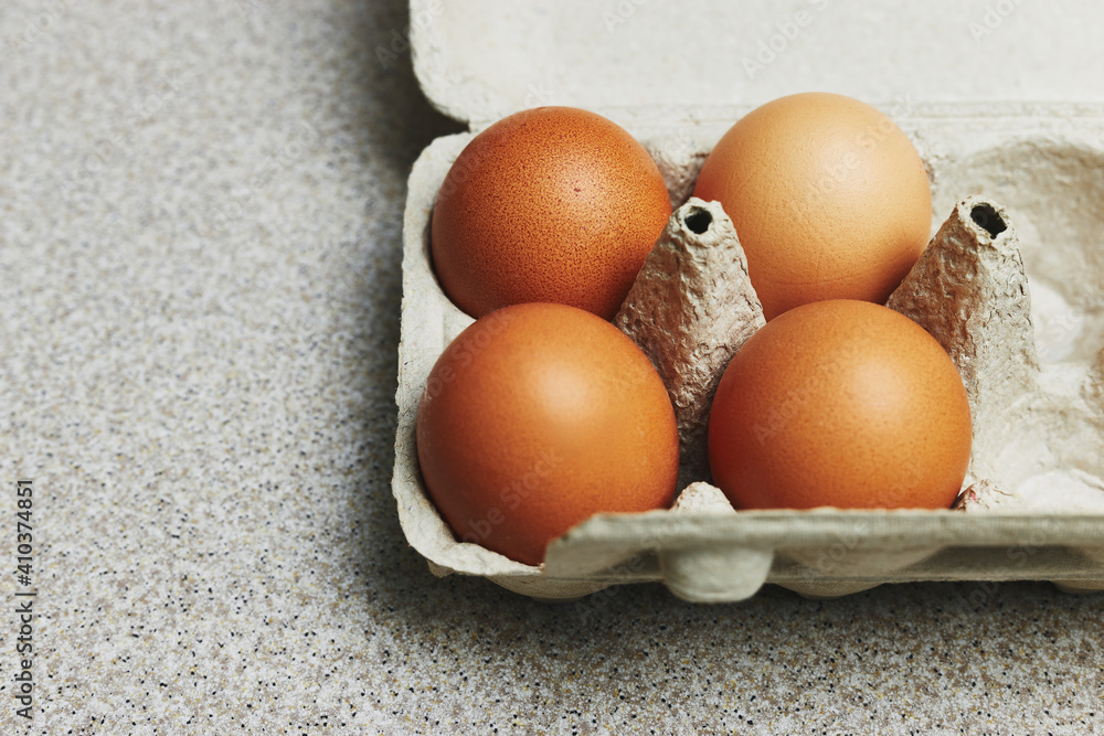 Wall mural Culinary class in a kitchen. Four tinted brown chicken eggs in an open carton box on the table ready for cooking. Close-up view.