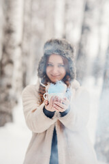 A girl in a hat with earflaps with a mug with steam. Walk in a birch grove in Siberia in winter. Young people of Russia.