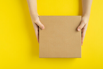 Craft box in hands on yellow background, top view. Copy space. Mock up.