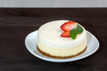 Delicate cheesecake cake with fresh strawberries and mint on white plate. Wooden background.
