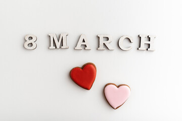 8 MARCH lettering and pink and red heart-shaped cookies on white background. Womens Day