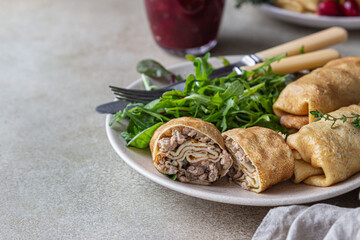 Homemade stuffed thin pancakes or crepes with meat, spicy cranberry sauce and arugula, light stone background. Traditional Russian cuisine for Maslenitsa. Shrove Tuesday.