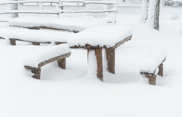 tables and benches covered in snow in winter city park, blizzard and snowfall
