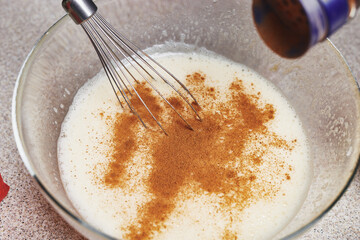Cinnamon is added to a transparent bowl with whipped eggs. Ingredients for baking cake. Cooking set. Mixer. Culinary class in a kitchen.