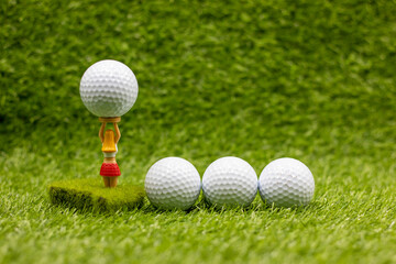 Golf balls are on green grass and one is on tee 
