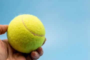 Hand is holding tennis ball on blue background