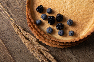Top view of empty tart shell decorated with berries and dried bent on wooden table 