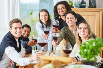Happy friends celebrating with a glass of red wine at home