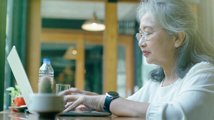 Active senior retired Asian business woman enjoy working on her own online small business and relaxing in a coffeeshop on a bright sunny day