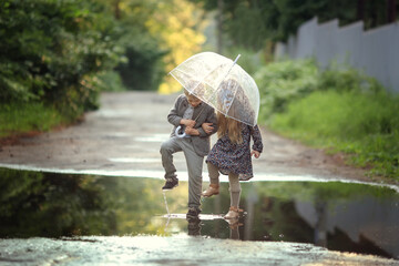 girl with long blond hair and a boy holding umbrella and jumping in puddles