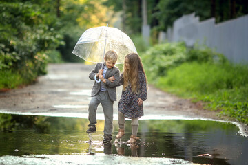 beautiful girl with long hair in dress and boy in a suit holding an umbrella walking in puddles after rain