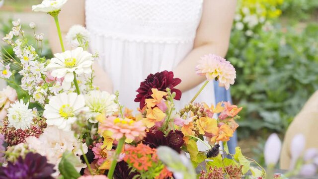 Unrecognizable woman hands cut colorful fresh flowers in metal bucket at wooden table in greenhouse at floral masterclass , close-up detail shot