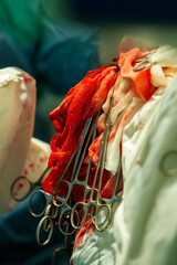 on bloody medical bandages, surgical clamps hang down to fix the thread for suturing the wound. close-up.