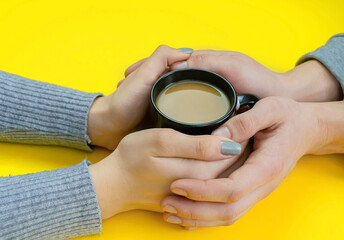 Hands on a yellow background with coffee, love. Coffee with milk, black cup. Selective focus.