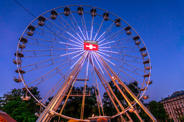 Bottom view of Swiss Ferris Wheel with flag of switzerland by night. Night view of Geneva cityscape in French Swiss, Switzerland.