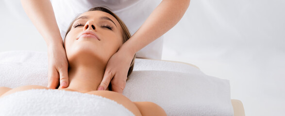 Masseur doing neck massage to client with closed eyes in spa salon, banner