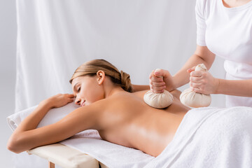 Woman massaging young client with herbal bags in spa salon