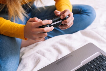 Young woman playing video game with laptop sitting on bed