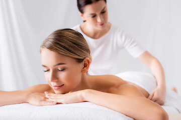 Obraz na płótnie Canvas Young woman lying on massage table near masseur on blurred background