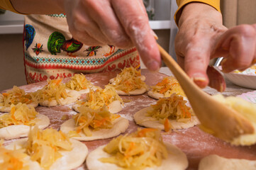 A woman fills small raw dough cakes with cabbage filling. Homemade baking