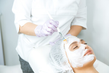 Facial skin care and protection. A young woman at a beautician's appointment. The specialist applies a cream mask to the face