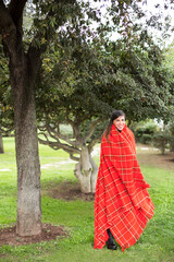 ragazza mora si copre per ripararsi dal freddo con un plaid rosso a quadri in un parco.