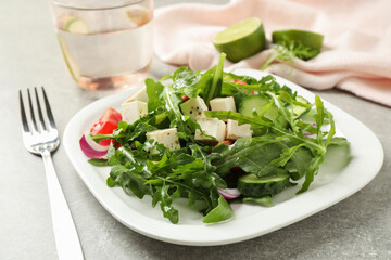 Delicious salad with feta cheese, arugula and vegetables on grey table, closeup