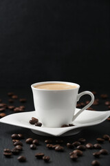 White cup of coffee on a black background. Close-up side view. Vertical photography. Coffee beans on a black table.