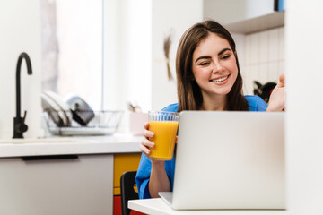 Happy brunette girl gesturing while using laptop and drinking juice