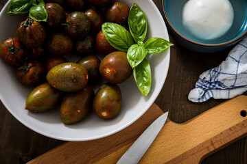 Gestreifte bunte Tiger Tomaten in Schale mit Mozzarella und Basilikum mit Geschirrtuch und Messer auf Holz Brett 