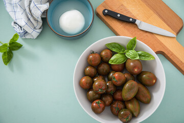 Gestreifte bunte Tiger Tomaten in Schale mit Mozzarella und Basilikum mit Geschirrtuch, Messer, Holz Brett auf Hintergrund Mint Grün