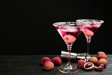 Lychee cocktail on dark wooden table against black background, space for text
