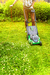 Man cutting green grass with lawn mower in backyard. Gardening country lifestyle background. Beautiful view on fresh green grass lawn in sunlight, garden landscape in spring or summer season.