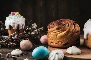 Easter cakes and painted eggs next to a willow wreath on a dark brown wooden table copy space.