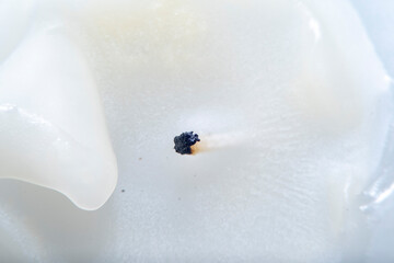 A burnt white, thick candle with molten paraffin wax. Close-up blurred in soft focus at high...