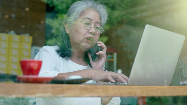 Active senior retired Asian business woman enjoy working on her own online small business and relaxing in a coffeeshop on a bright sunny day