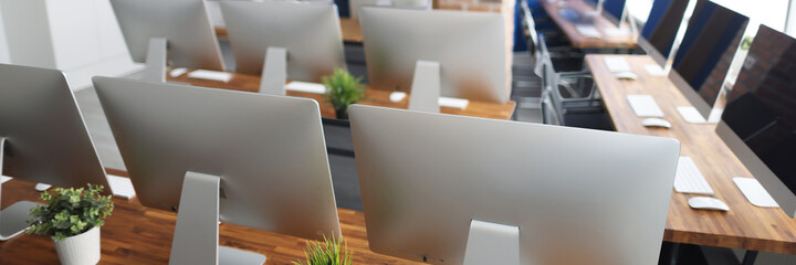 Many silver monitors stand on a wooden table in office closeup. Programmer professional education...