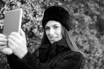 ragazza con il colbacco nero si fa un selfie con un tablet in un parco