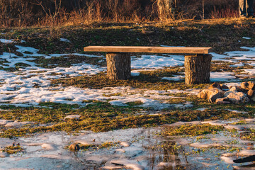 An old wooden bench on a clearing covered with melting snow on a sunny day.